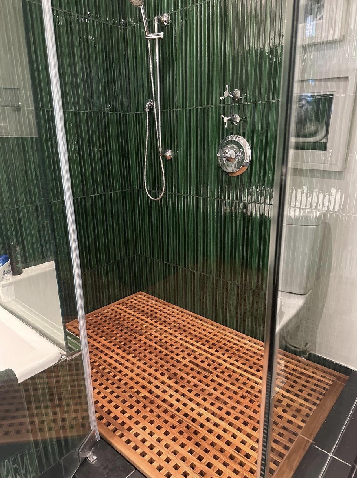 Warm teak lattice shower mat set against deep green shower tiles.