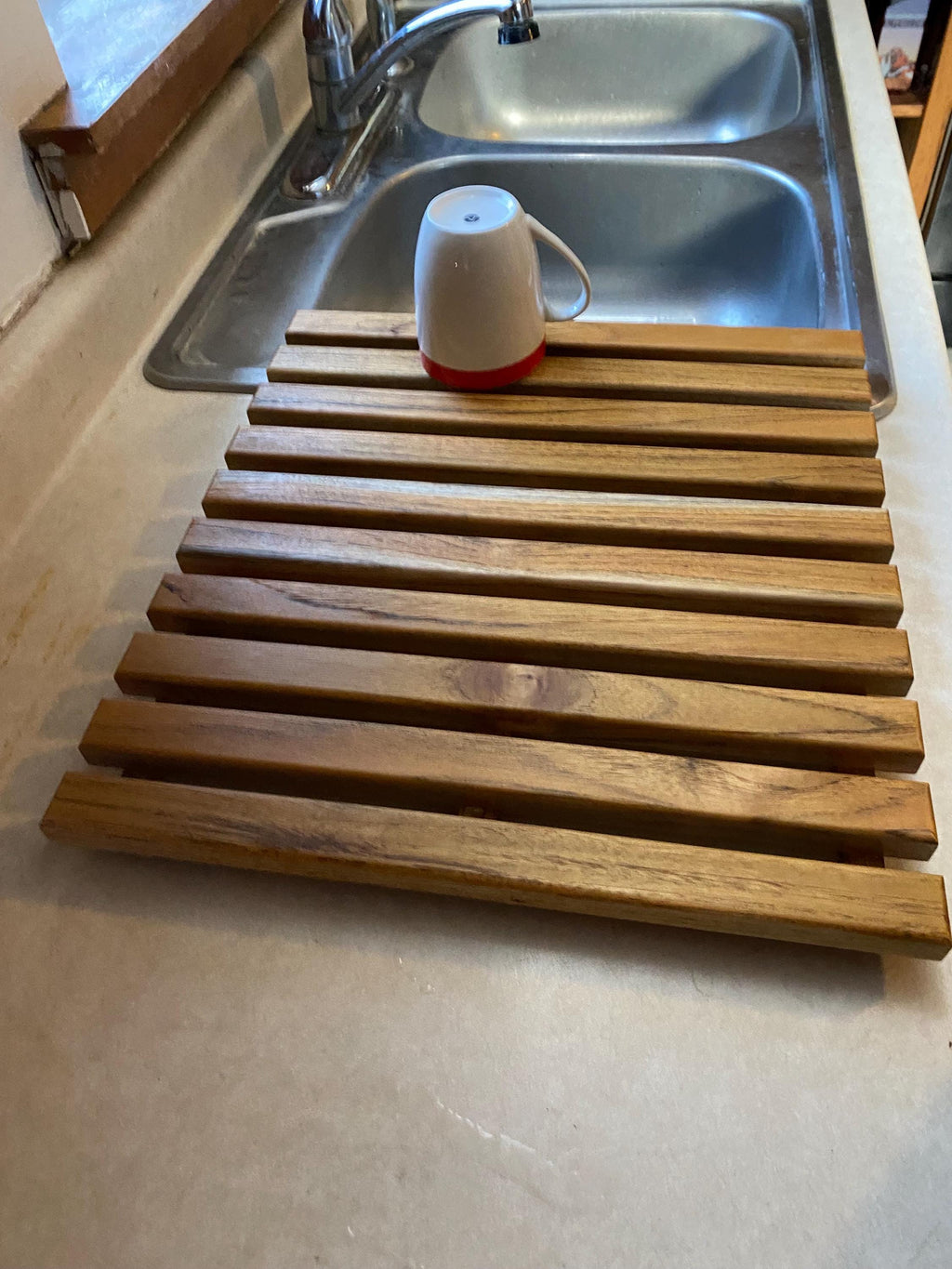 Teak dish drying rack holding a cup on a counter