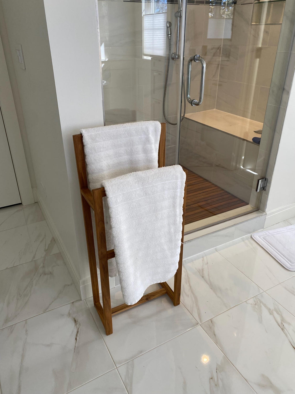Solid teak towel rack mounted on a bathroom wall with towels