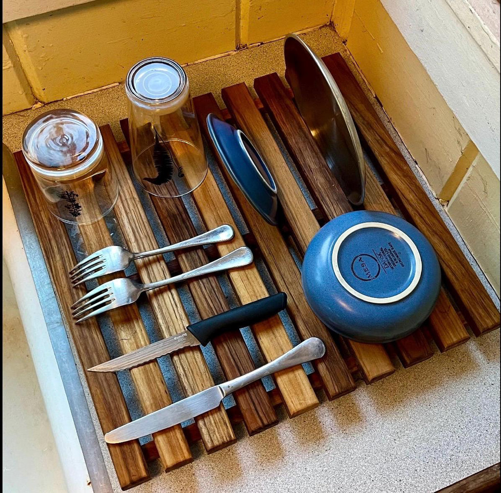 Teak dish drying rack holding bowls, plates, cups, silverware from top