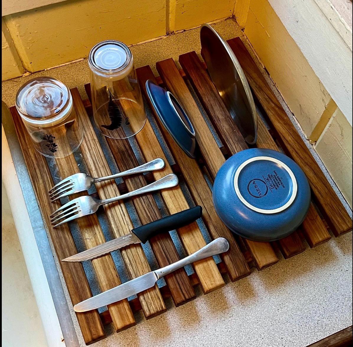 Teak dish drying rack holding bowls, plates, cups, silverware from top