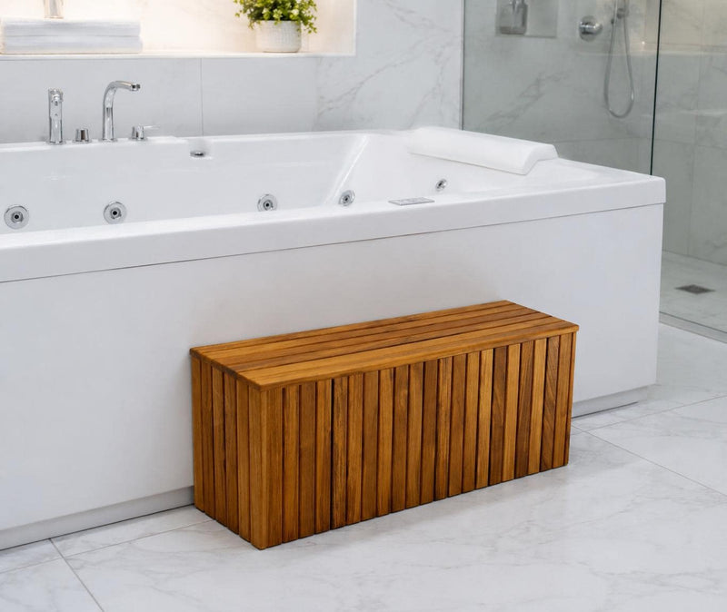 A rectangular wooden bench with vertical slats sits in front of a white hot spring bathtub in a modern bathroom with white marble tiles.