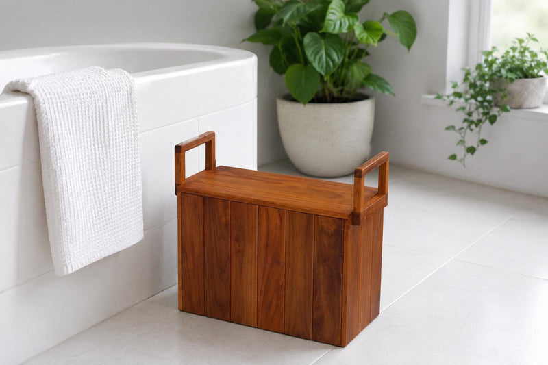 A rectangular wooden storage bench with a hinged lid and integrated handles, placed on a light tiled bathroom floor next to a white bathtub with a white towel draped over the edge.