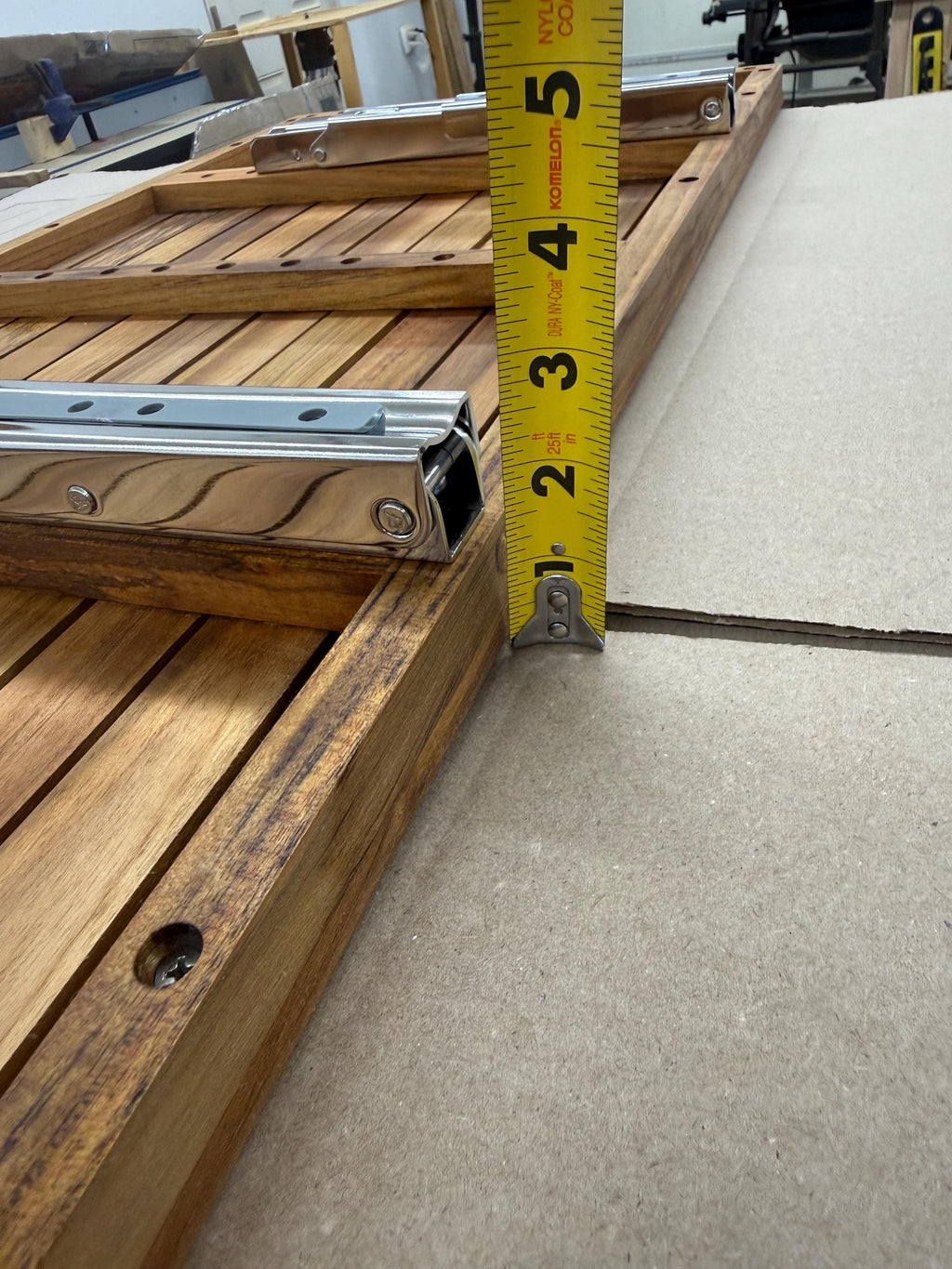 Close-up of the teak bench frame with a yellow tape measure standing vertically to show the total depth of the bench.