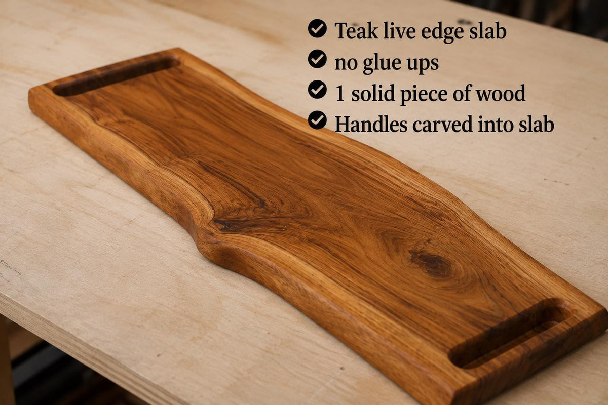 A teak live edge wood serving slab with integrated handles, displayed on a light wood workbench with a text overlay detailing its features.